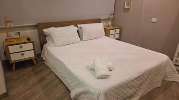 A neatly made bed with a quilted bedspread, two bedside tables with lamps, and a wooden floor.