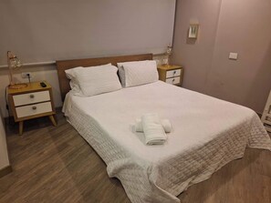 Ein ordentlich bezogenes Bett mit einer gesteppten Tagesdecke, zwei Nachttische mit Lampen und ein Holzboden.