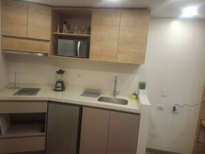 A kitchen with wooden cabinets, a microwave, a blender, a sink, and a small potted plant. - Lourdes Executive Suites 204 (Bogotá)