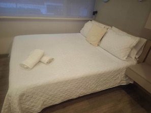 A neatly made bed with a quilted cover, two rolled towels, and a bedside table. - Lourdes Executive Suites 204 (Bogotá)