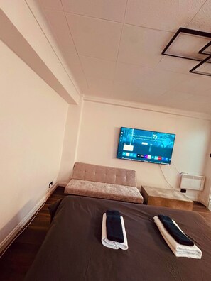 Een hotelkamer met een bed, een aan de muur bevestigde televisie en een klein zithoekje.