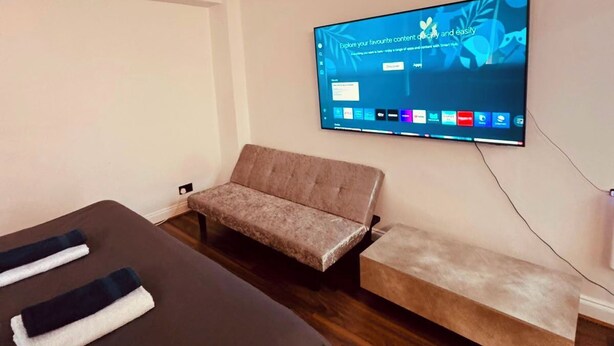 Ein Hotelzimmer mit Bett, einer Sitzecke, einem an der Wand befestigten Fernseher und Holzboden.