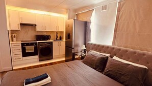 Ein Schlafzimmer mit einem großen Bett, einer separaten Küchenzeile und einem Fenster mit Vorhängen.