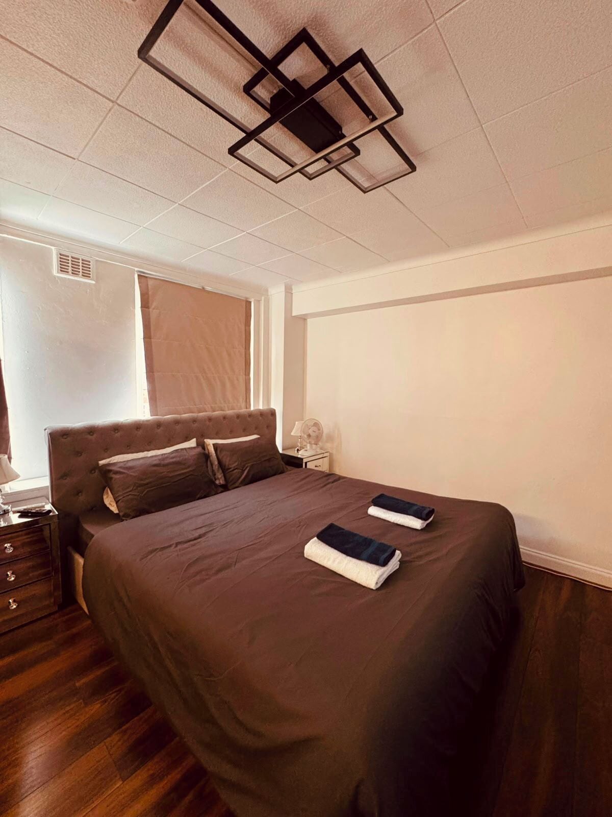 A bedroom with a large bed, a nightstand, a lamp, and a ceiling light fixture.