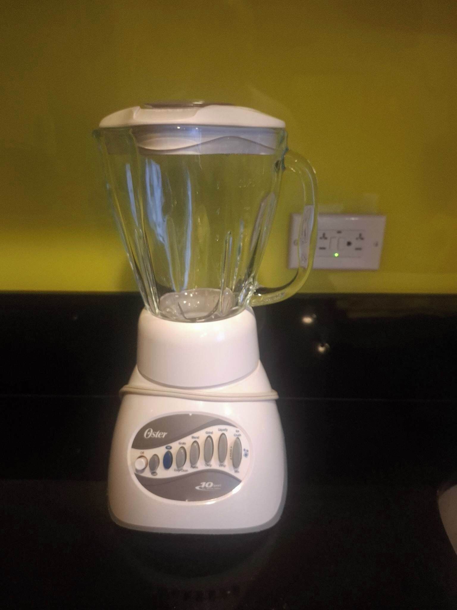 Una licuadora Oster blanca sobre una encimera de cocina con una pared amarilla al fondo.