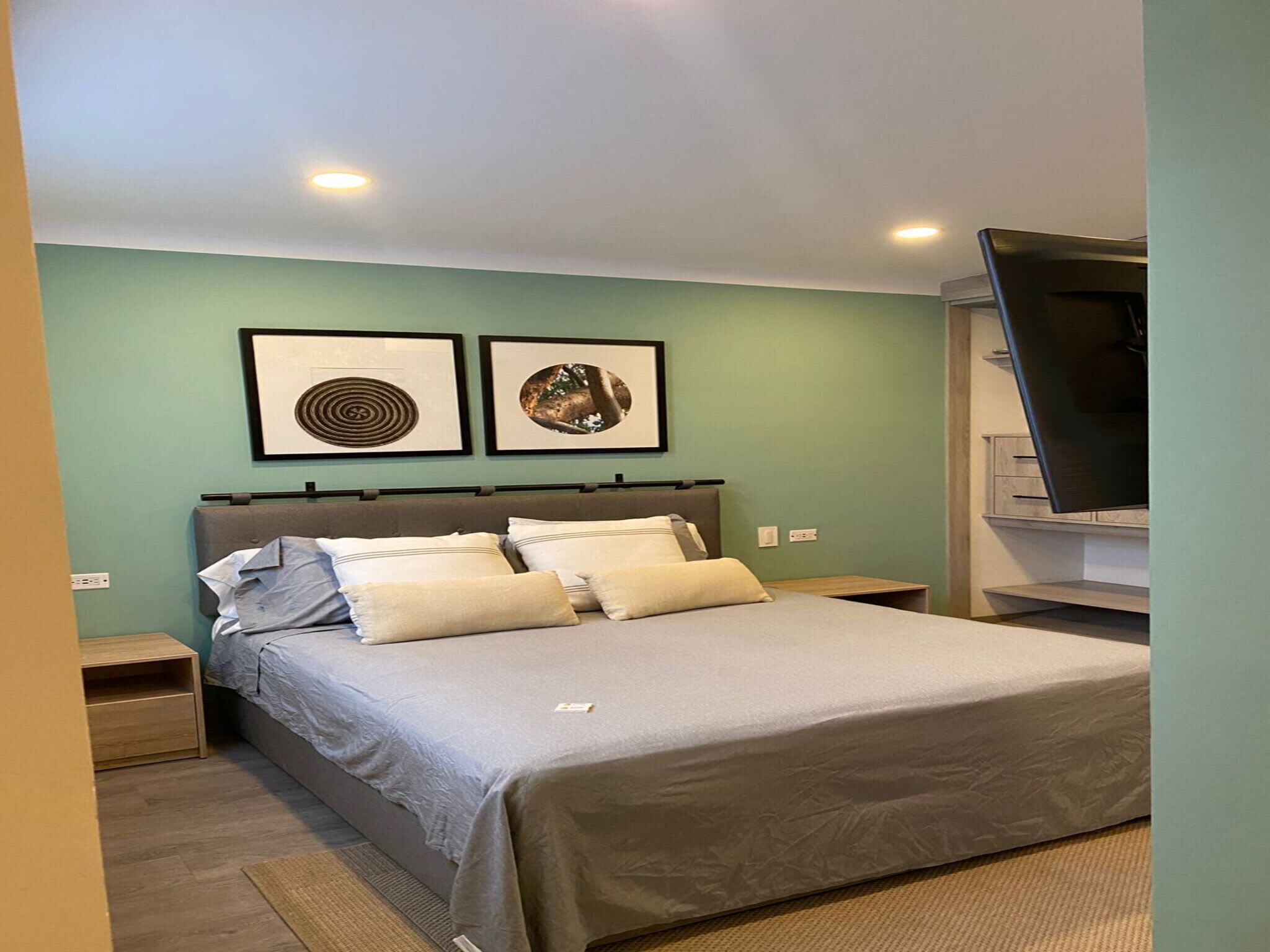 A bedroom with a bed, two nightstands, a flat-screen TV, and two framed pictures on the wall.