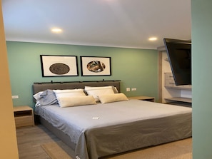 Ein Schlafzimmer mit einem Bett, zwei Nachttischen, einem Flachbildfernseher und zwei gerahmten Bildern an der Wand.