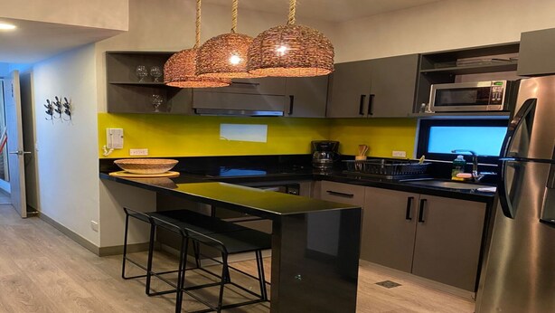 Una cocina moderna con una isla central, taburetes de bar, un refrigerador de acero inoxidable y un microondas.