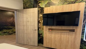 Un dormitorio con cama, televisor montado en un mueble de madera y un mural en la pared.