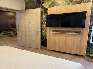 Ein Schlafzimmer mit Bett, einem an einer Holzeinrichtung montierten Fernseher und Wandmalerei.