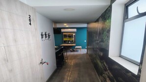 Un pasillo con suelo de madera, una puerta con la etiqueta '204', un ventanal con vistas a un bosque y una pared con un mural.