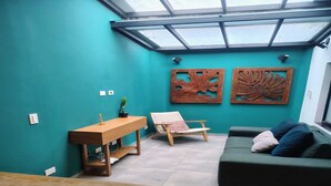 Una habitación con tragaluz, un escritorio de madera, una silla, un sofá y dos obras de arte en las paredes.