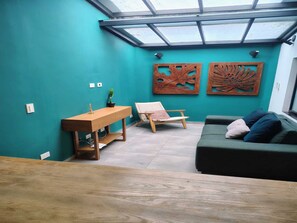 Ein Zimmer mit Oberlicht, einem Holztisch, einem Stuhl, einer Couch und zwei Wandbildern.