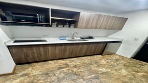 A compact kitchen with a built-in microwave, a sink, and wooden cabinets. - Laureles Executive Suites 104 (Medellín)