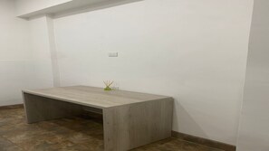 Ein Zimmer mit einem Holztisch, einem kleinen, grünen Blumenvasen mit Schilfrohren und einer weißen Wand mit Steckdose.