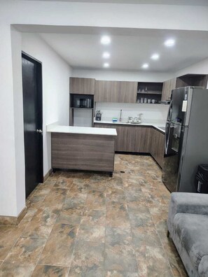 A compact kitchen with a central island, built-in appliances, and a dark-toned floor. - Laureles Executive Suites 105 (Medellín)