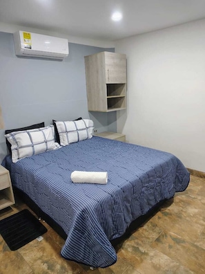 A bedroom with a bed, pillows, a bedside table, a nightstand, a wardrobe, and an air conditioning unit. - Laureles Executive Suites 105 (Medellín)