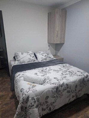 Ein Bett mit floralem Bettbezug, ein Holzschrank und ein Nachttisch mit Lampe.