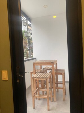 A room with a wooden table and chairs, a window with a view of buildings, and a door with a light switch. - Laureles Executive Suites 202 (Medellín)