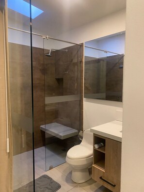 A modern bathroom with a glass shower enclosure, a toilet, and a vanity with a mirror. - Laureles Executive Suites 202 (Medellín)
