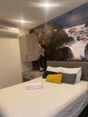 A bedroom with a bed, a nightstand, a wardrobe, and a large wall mural of a rocky landscape. - Laureles Executive Suites 202 (Medellín)