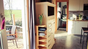 Une terrasse en bois avec une chaise, un meuble de rangement intégré doté de tiroirs et une vue sur un champ verdoyant.