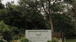 A sign for 'MUCHENJE River Lodge' with a gate and surrounding greenery.