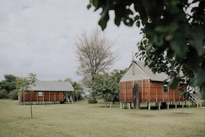 Dos edificios rústicos de madera con techos de metal, rodeados de hierba y árboles.