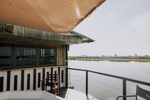 A boat with a wooden deck, a chair, and a large umbrella. - Muchenje River Lodge  (Katima Mulilo)