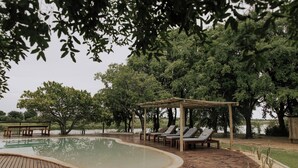 Una terraza de madera con piscina, sillas de descanso y un pérgola.