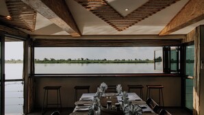 Un comedor con una mesa preparada para cuatro, ventanas amplias y vista a un cuerpo de agua.