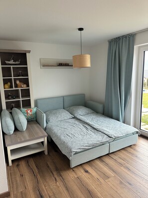 Une chambre moderne avec un lit, un petit coin salon, une étagère avec des objets décoratifs et une fenêtre avec des rideaux.