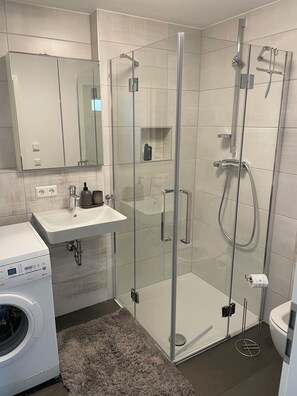 Une salle de bain moderne avec une douche à parois de verre, un lavabo et un lave-linge.