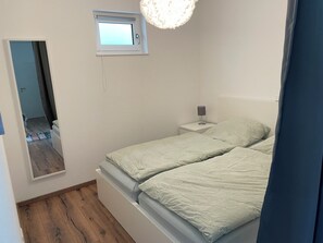 Une chambre à coucher avec un lit, une table de chevet, une lampe, une fenêtre et un miroir.