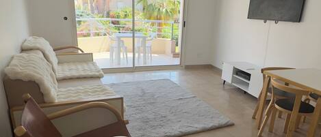 Un salón espacioso con sofá, una silla de madera, televisor montado en la pared y puertas de vidrio corredizas que dan a un patio exterior.