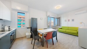 Eine moderne Küche mit Esstisch, Stühlen und einem grünen Sofa in einem hellen Wohnbereich mit großen Fenstern.