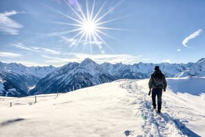 Eine Person geht auf einem mit Schnee bedeckten Weg, im Hintergrund Berge.