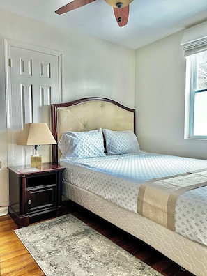 Quarto com cama, mesa de cabeceira, abajur e janela.