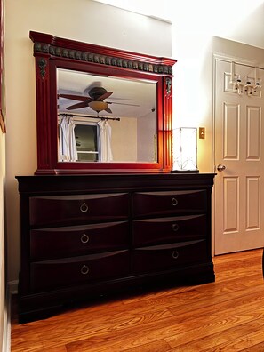 Une commode en bois foncé, dotée d’un grand miroir, d’un ventilateur de plafond et d’une porte avec un porte-manteau.