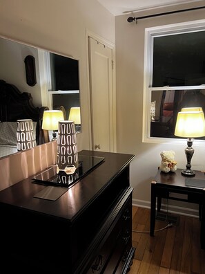 A room with a dark wooden dresser, a mirror, a bedside table with a lamp, and a window. - 3 Bdrm Aloha home Falls Church (Falls Church)