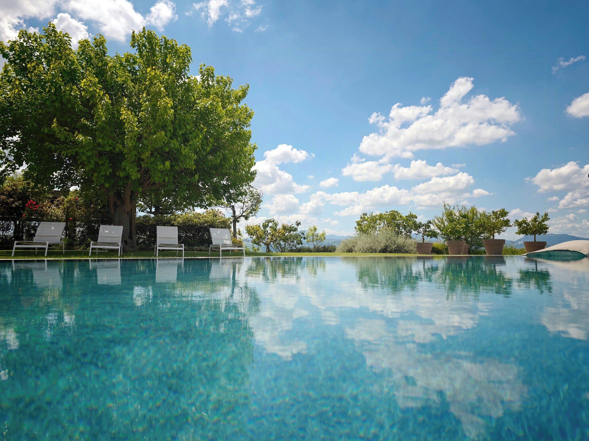 A clear swimming pool with lounge chairs and trees in the background.
