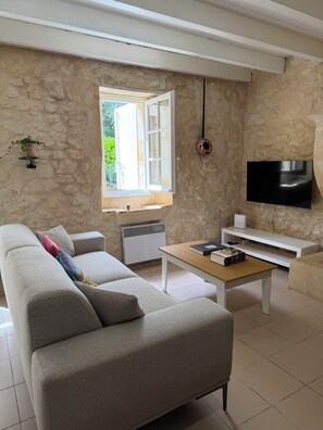 Ein Wohnzimmer mit einer Couch, einem Couchtisch, einem Fernseher und einem Fenster mit geöffnetem Klappladen.