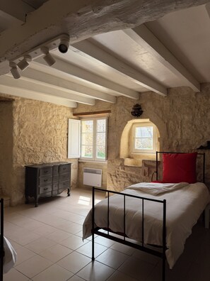 A bedroom with a bed, a dresser, a window, and a stone wall. - Charming stone house near Saint-Émilion (Lugaignac)