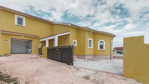 A yellow building with a garage, a covered entrance, and a gated area. - Spacious 4-bedroom Villa in marvellous Pula with  outdoor kitchen and Pool (Pula)