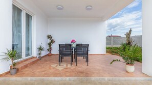 Eine überdachte Terrasse mit Tisch und Stühlen, Blumentöpfen und Blick auf die Umgebung.