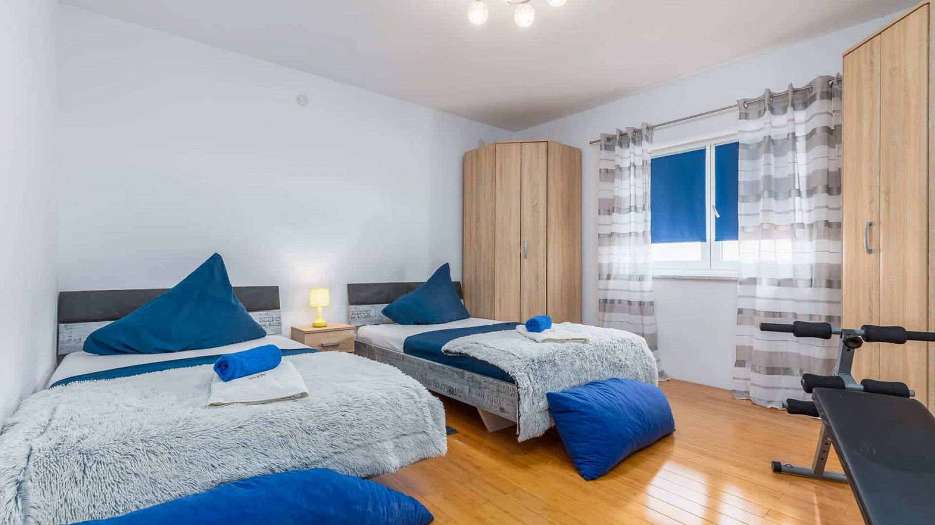 Ein Schlafzimmer mit zwei Betten, einem Kleiderschrank, einem Fenster mit Vorhängen und einer Bank.