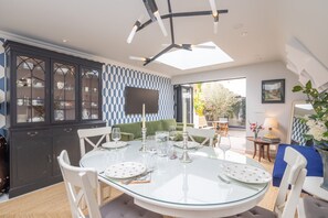 A dining area with a glass table, white chairs, a dark cabinet with glass doors, and a patterned wall. - Beautiful Cambridge Home by Midsummer Common (Cambridgeshire)