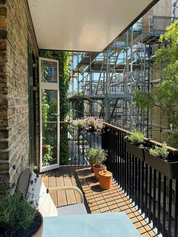 A balcony with a wooden floor, potted plants, and a view of a building under construction.