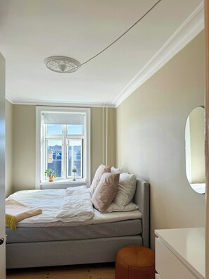 Ein Schlafzimmer mit Bett, Fenster mit Blick, Nachttisch und Spiegel.