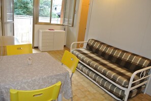 A room with a dining table, yellow chairs, a plaid sofa, and a radiator. - Cozy flat with pool just 50m from the beach (Lignano Sabbiadoro)
